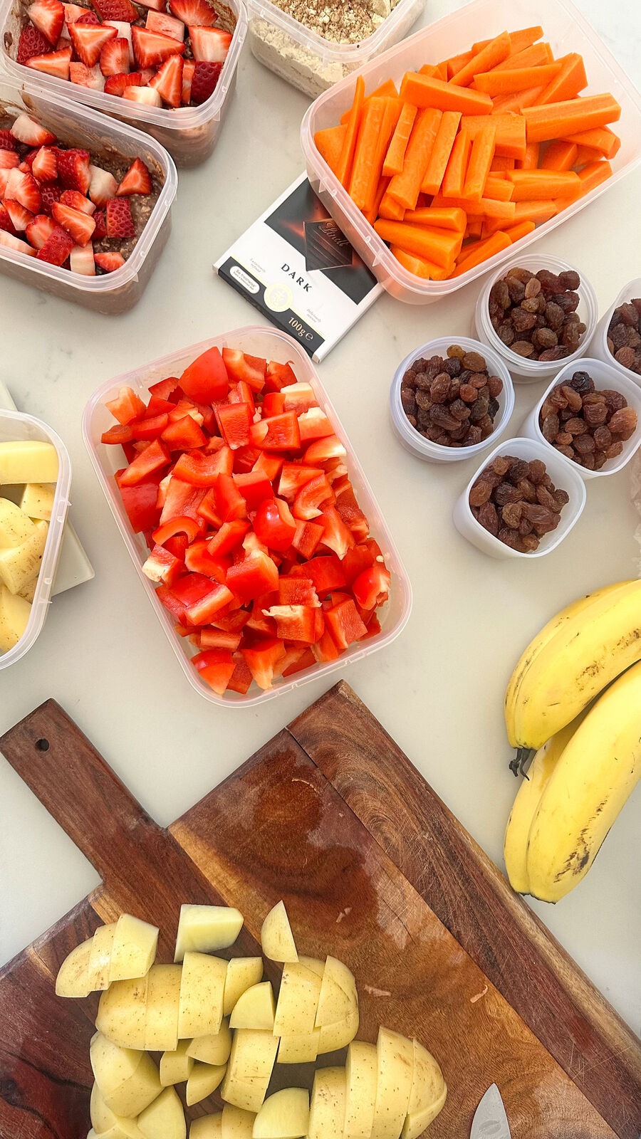 Containers of prepped strawberries, carrots, capsicum, potatoes and fruit on a bench